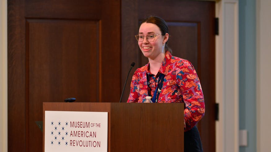 Clare McCabe discusses the Davenport baby booties at the Conference on Collecting the American Revolution while standing at a podium with the Museum logo on the front.