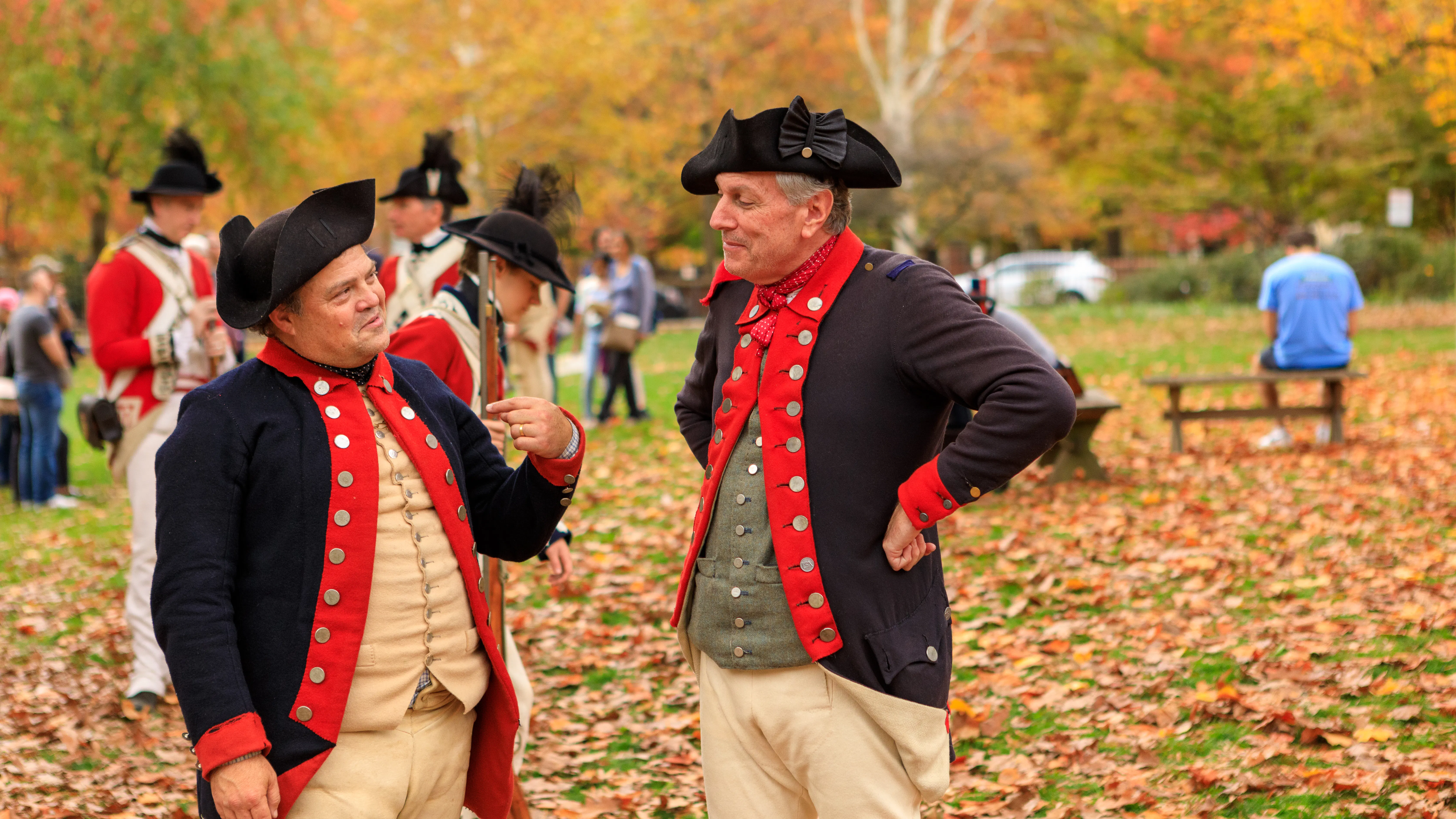 Two costumed interpreters stand in front of fall trees