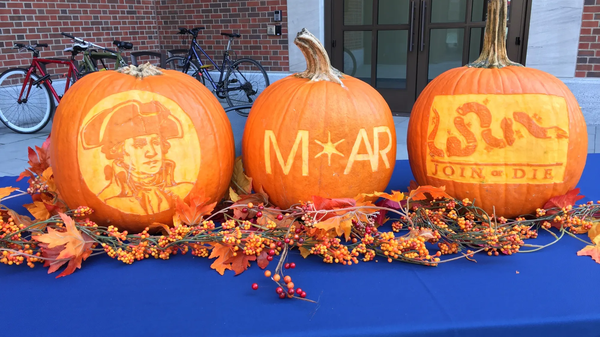 Three carved pumpkins on a table with a festive garland and a blue tablecloth