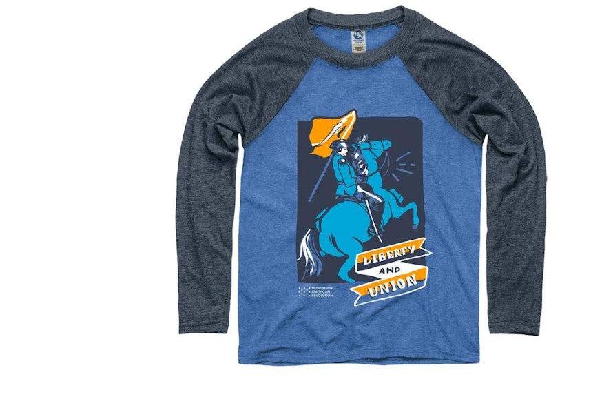This long-sleeve youth baseball t-shirt features a blue torso with grey sleeves, the words Liberty and Union, and the image of a man carrying a flag while on a horse.