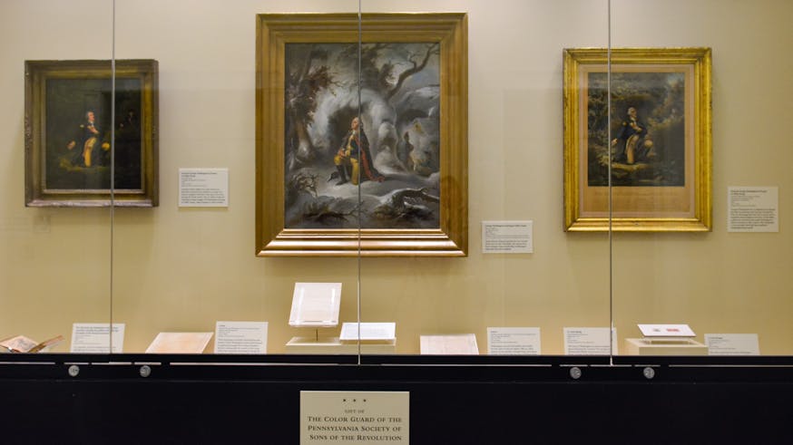 A display of three paintings, three letters, a book, and stamps related to Washington's prayer at Valley Forge.