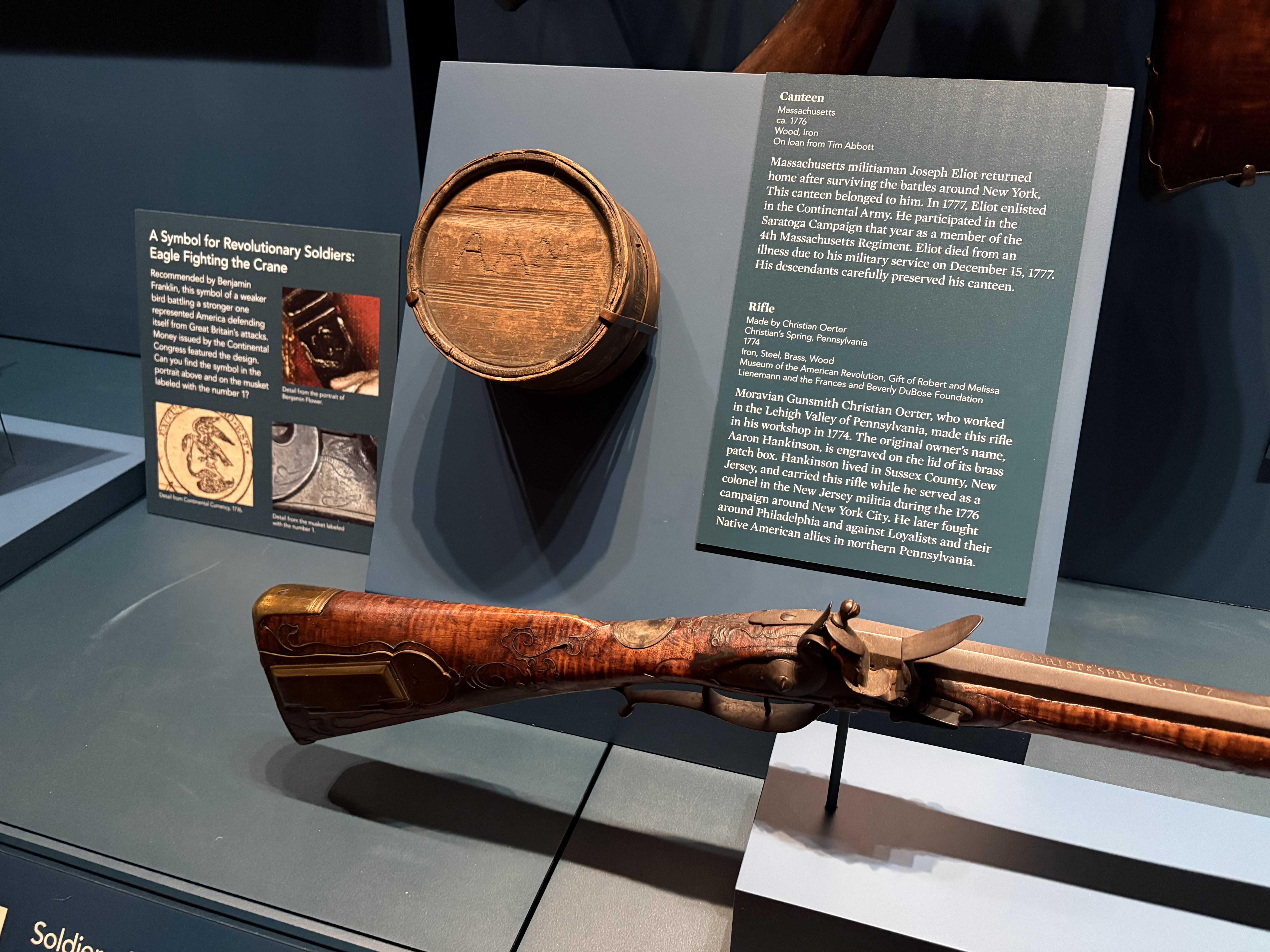 A display case featuring a wooden canteen and a rifle