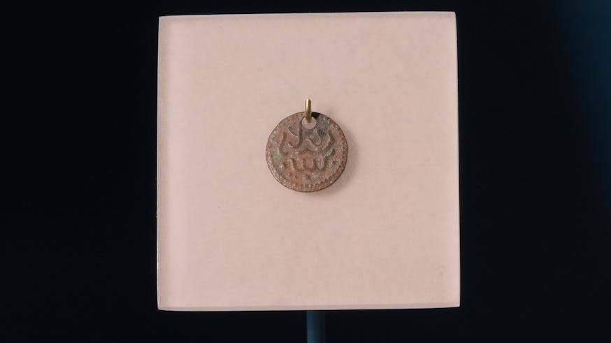 This small charm includes an Arabic phrase that translates to "No God but Allah"