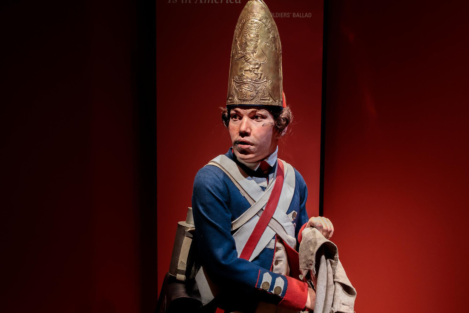 A lifesize figure of a soldier in 18th century clothes with a large gold helmet