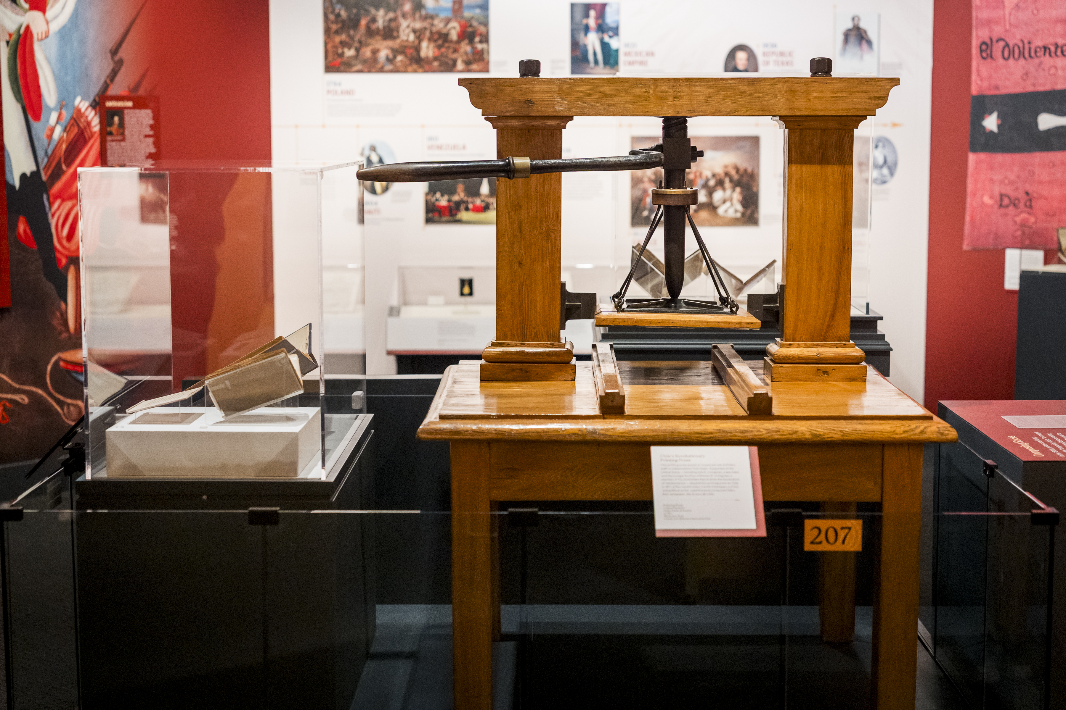 A large wooden printing press sitting next to a museum exhibit case with books displayed.