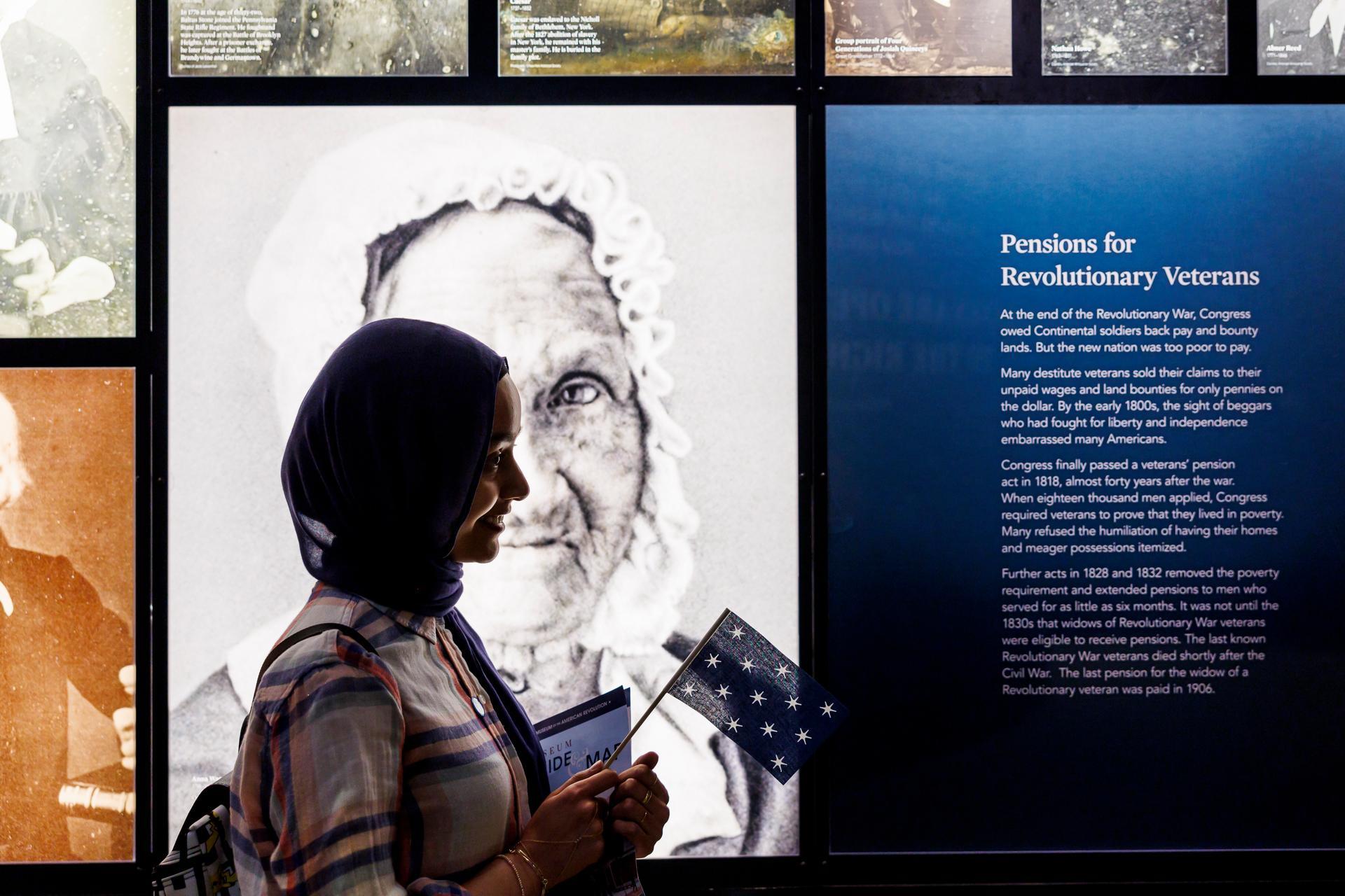 A person holding a flag stands in front of a wall of images in the galleries