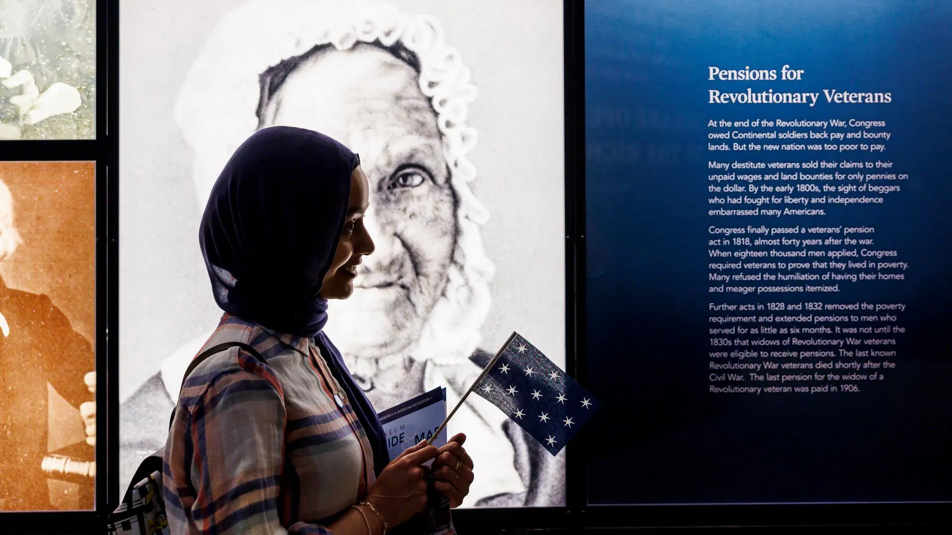 A person holding a flag stands in front of a wall of images in the galleries
