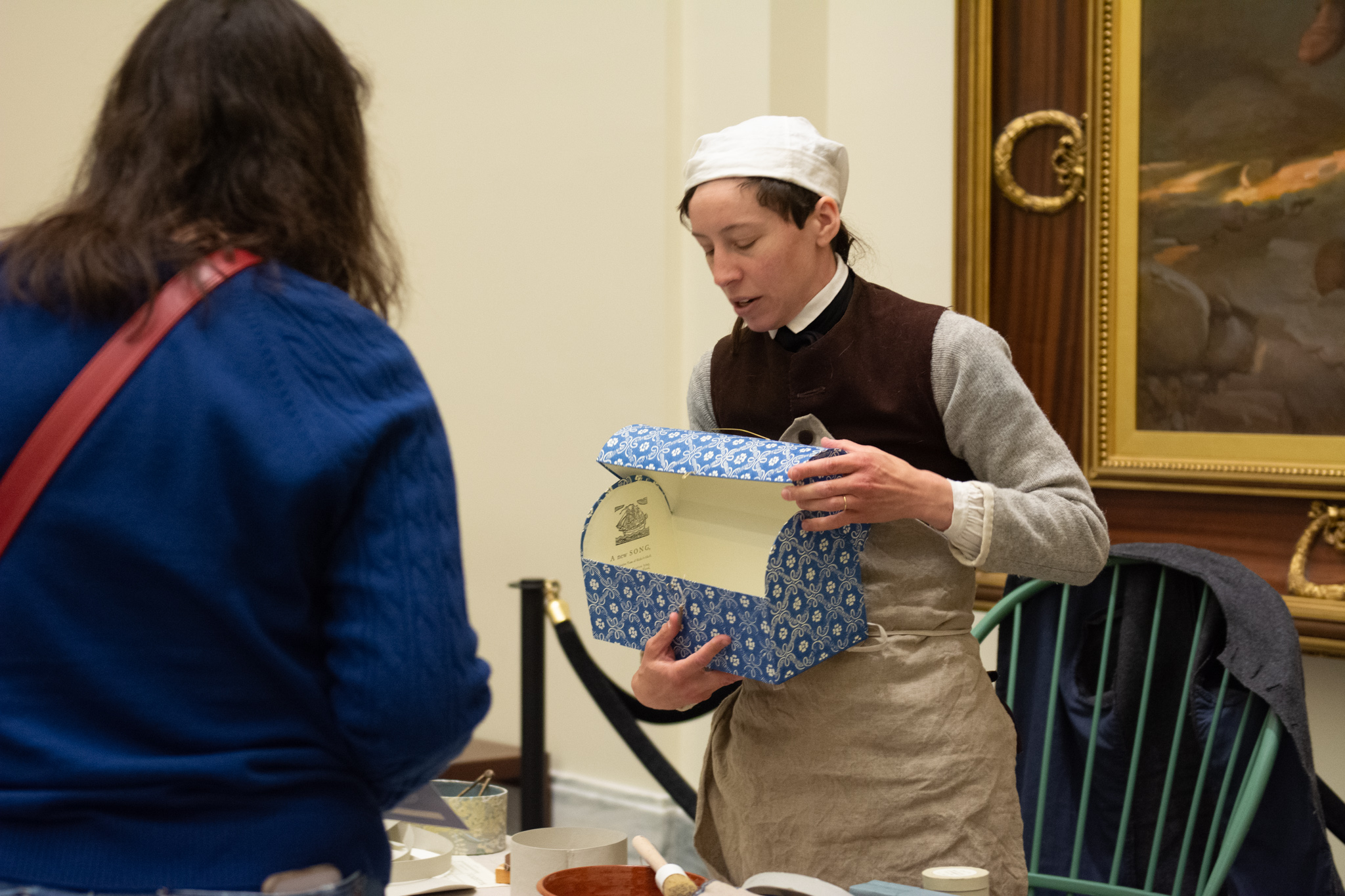 A costumed interpreter shows a visitor a blue patterned box