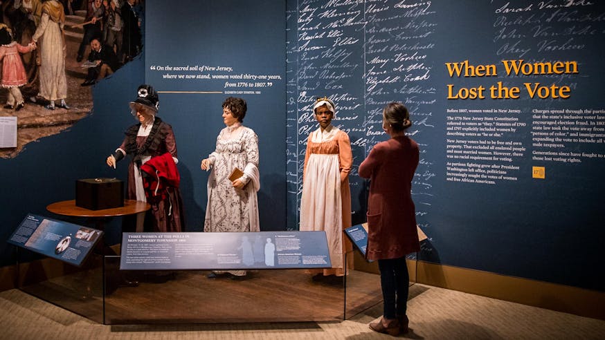 A visitor looks at the When Women Lost the Vote tableau featuring two white women and a woman of color voting in New Jersey in 1811.