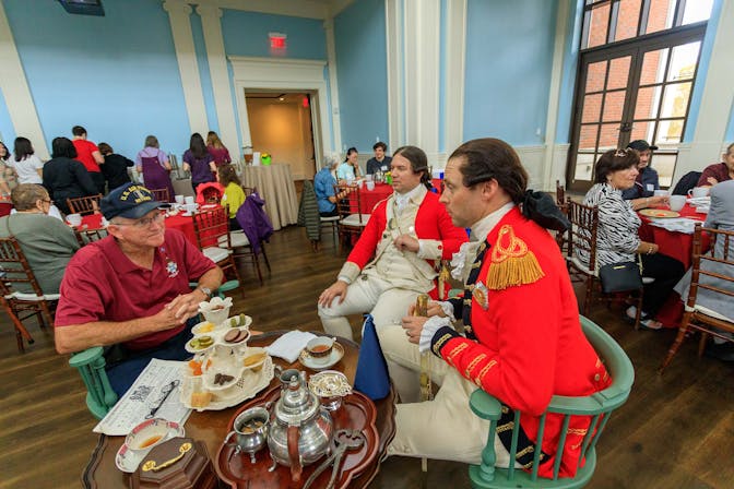A Museum Member talks to two costumed living historians dressed as British redcoats at the member teatime at Occupied Philadelphia.