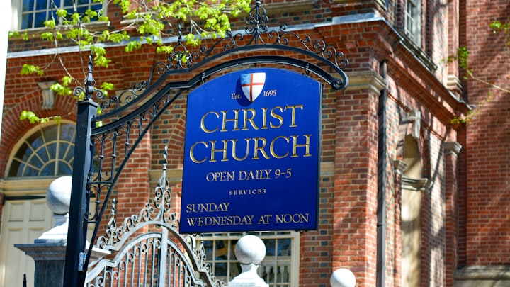 A blue sight with gold engraved text reads Christ Church Open Daily 9-5 hangs outside the church in Old City Philadelphia.