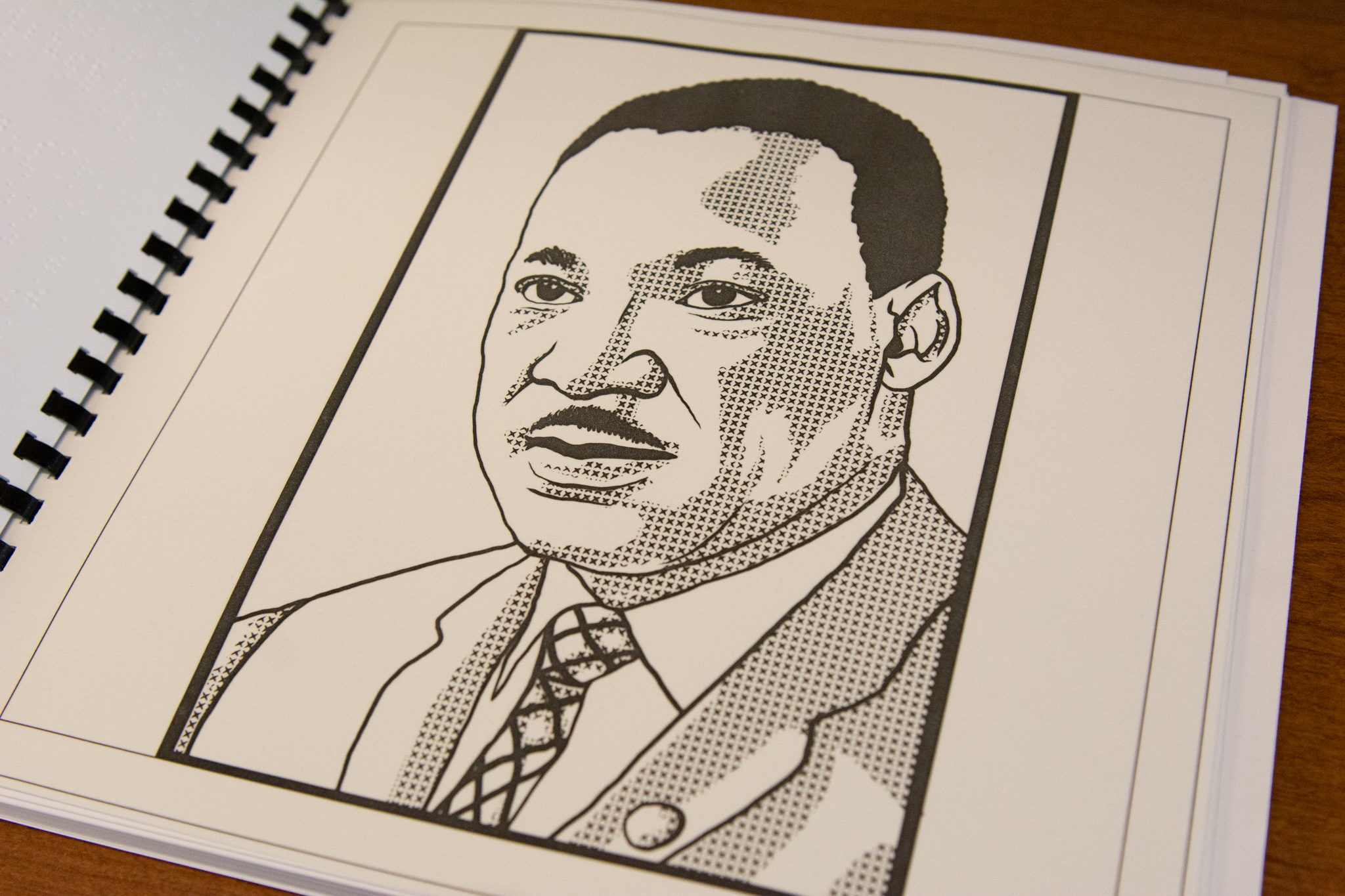 A book with black spiral binding open to a black and white image of a man