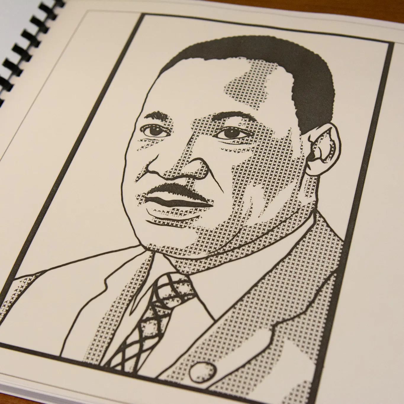 A book with black spiral binding open to a black and white image of a man