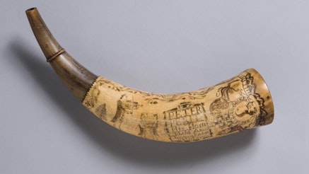 This image shows the powder horn of Peter Perit. The horn has illustrations of a king and his horse, as well as a violinist and two figures dancing.