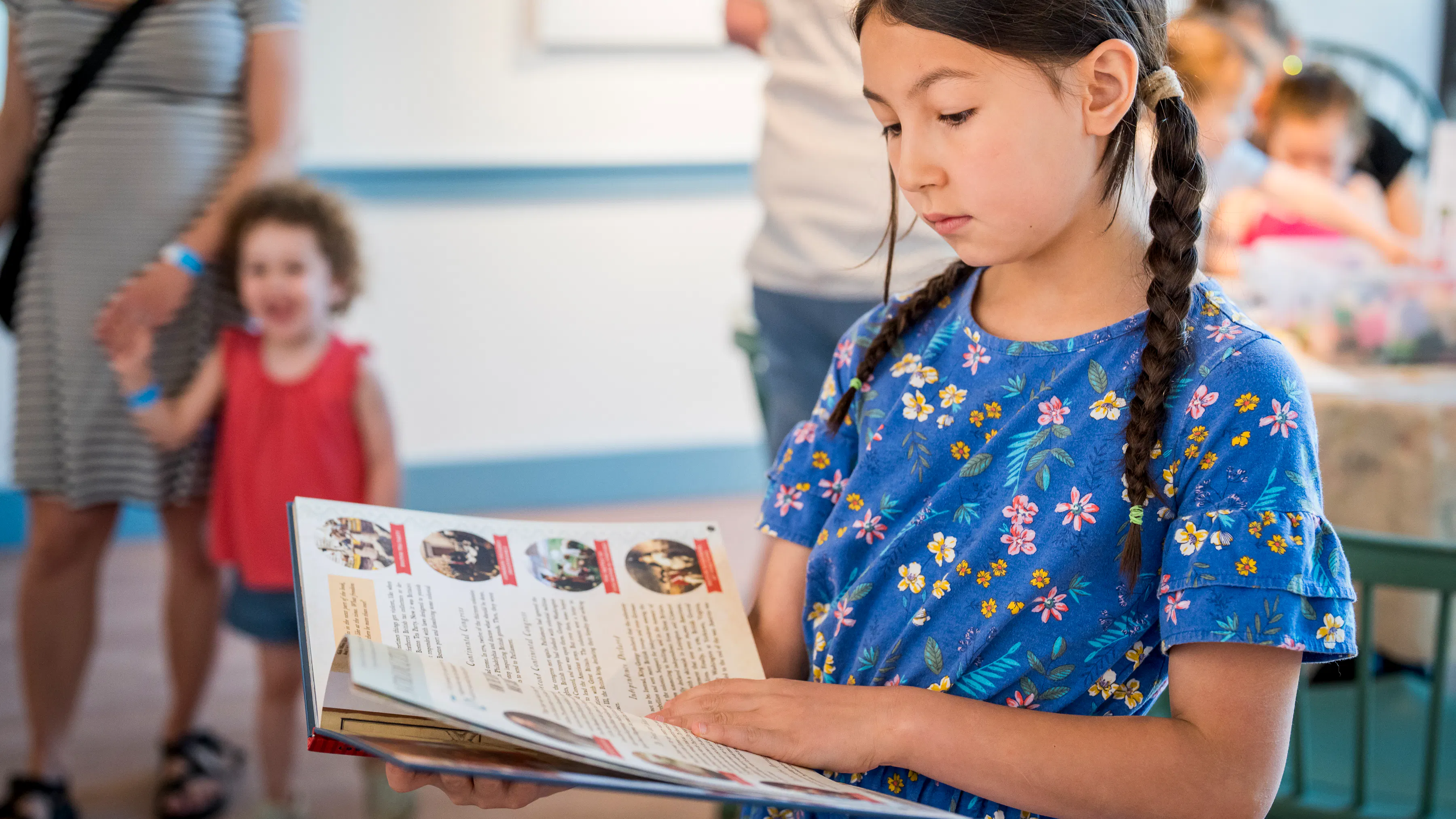 Young girl with long braided pigtails and blue shirt reads a picture book