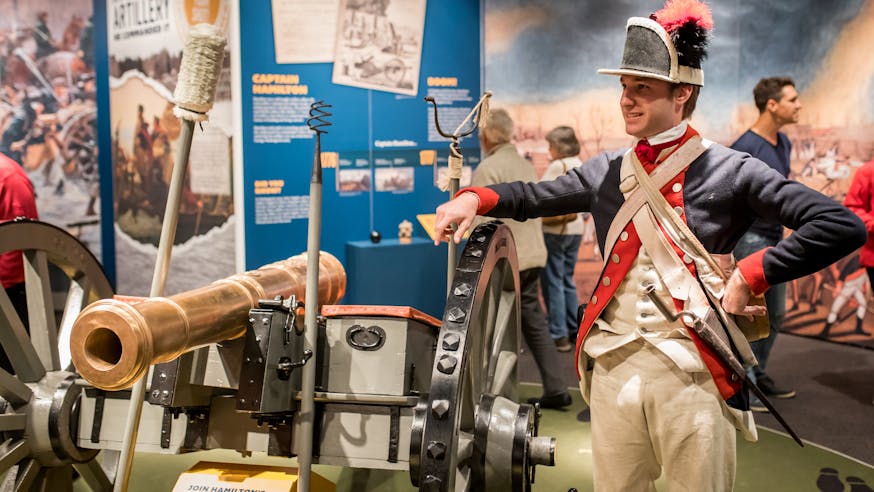 A male costumed Museum educator gives a demonstration about a cannon as part of the Hamilton Was Here exhibit.
