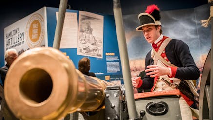 A male costumed Museum educator gives a demonstration about a cannon as part of the Hamilton Was Here exhibit.