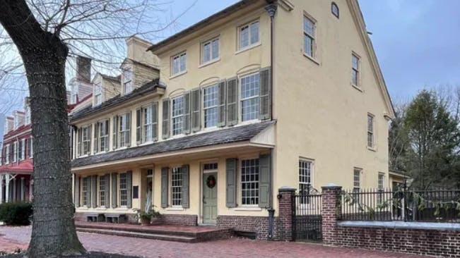 This image shows the exterior beige with olive green shutters building of the Indian King Tavern Museum.