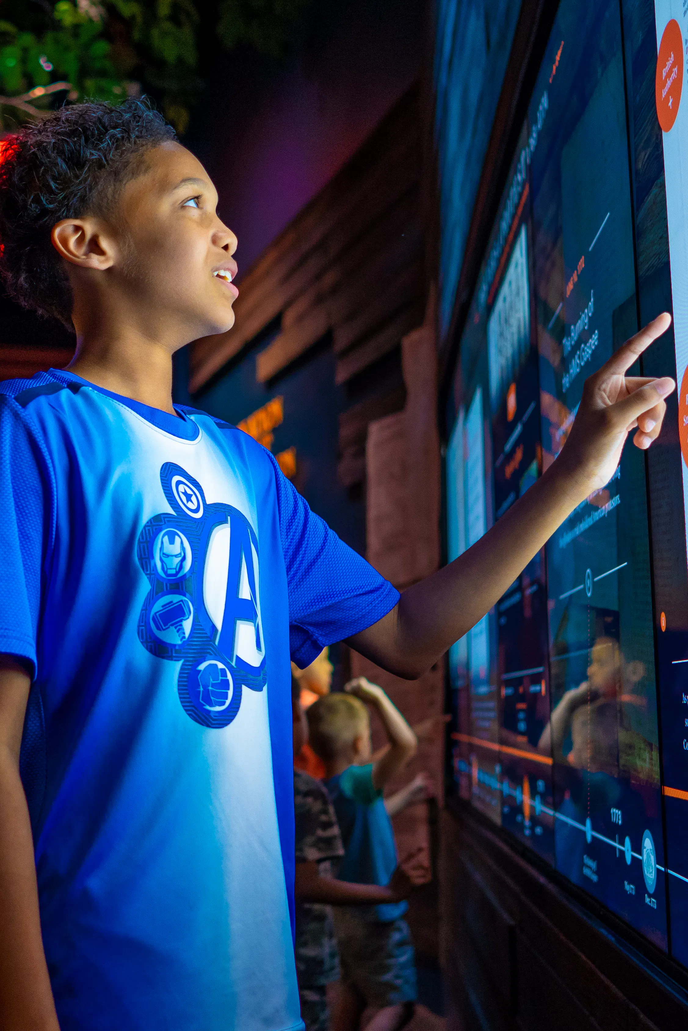 Kid in blue shirt interacts with Revolutionary War content touchscreen