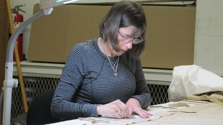 Textile conservator Virginia Whelan works sitting at a table on conserving a portion of George Washington's Revolutionary War tent.