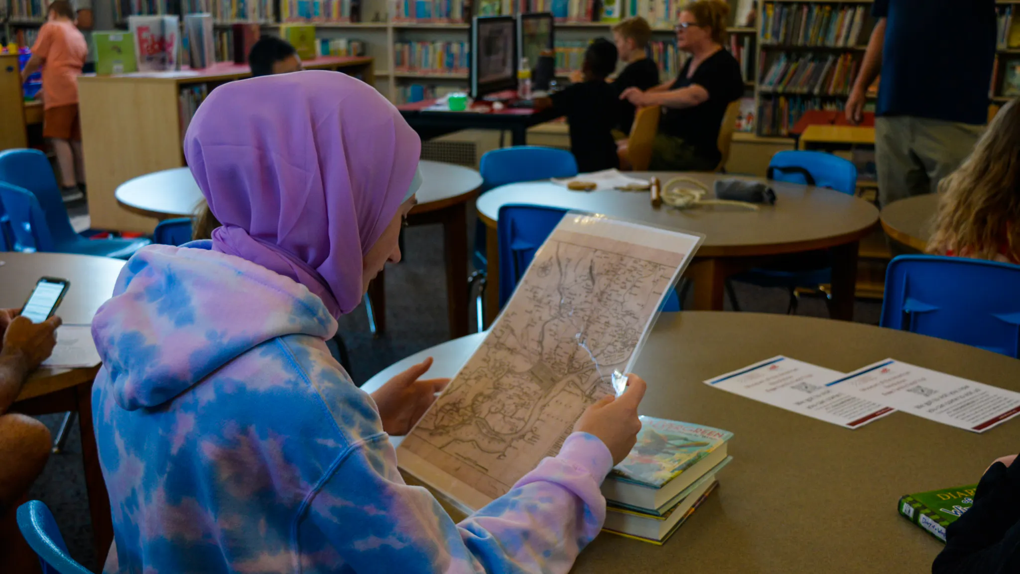 Girl wearing blue and pink hoodie looks at 18th-century style map