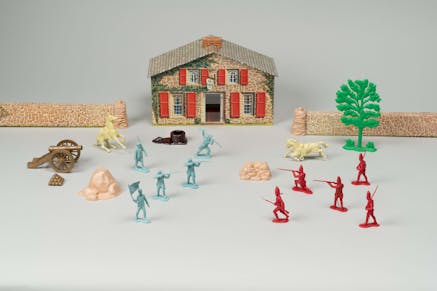 Blue and red toy soldier pieces in front of a toy recreated 18th century house.
