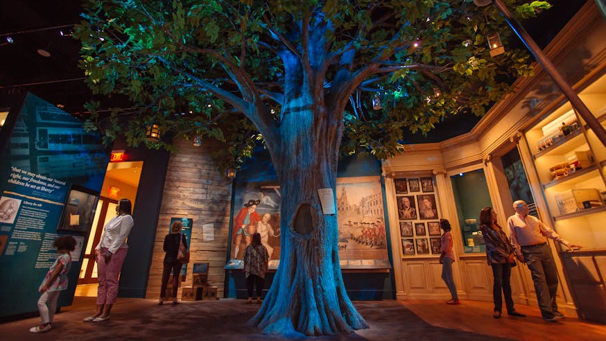 Visitors of the Museum of the American Revolution in the Liberty Tree gallery which features a Liberty Tree