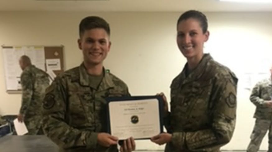 Matthew Midget, wearing camo military gear, receives a military certificate.