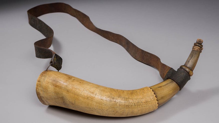 This image shows Abel Scott's Powder Horn. It is displayed against a white background. It is attached to a brown strap.