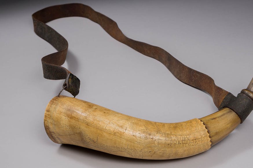 This image shows Abel Scott's Powder Horn. It is displayed against a white background. It is attached to a brown strap.