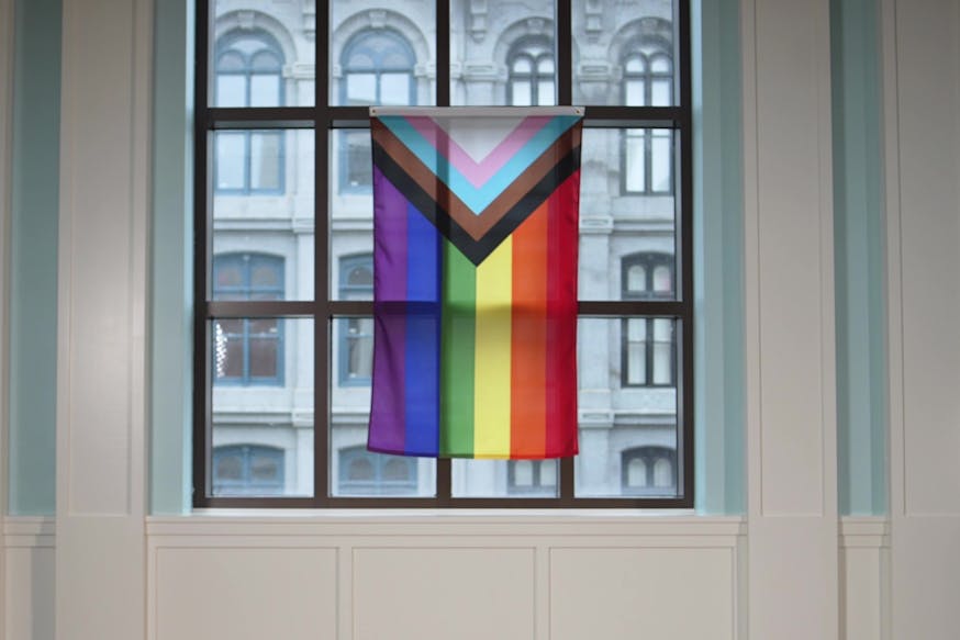 The Pride flag featuring rainbow stripes along with the striped in-cut triangle of white, pink, baby blue, brown, and black for transgender rights of all races hangs from a window in the Museum's Liberty Hall.