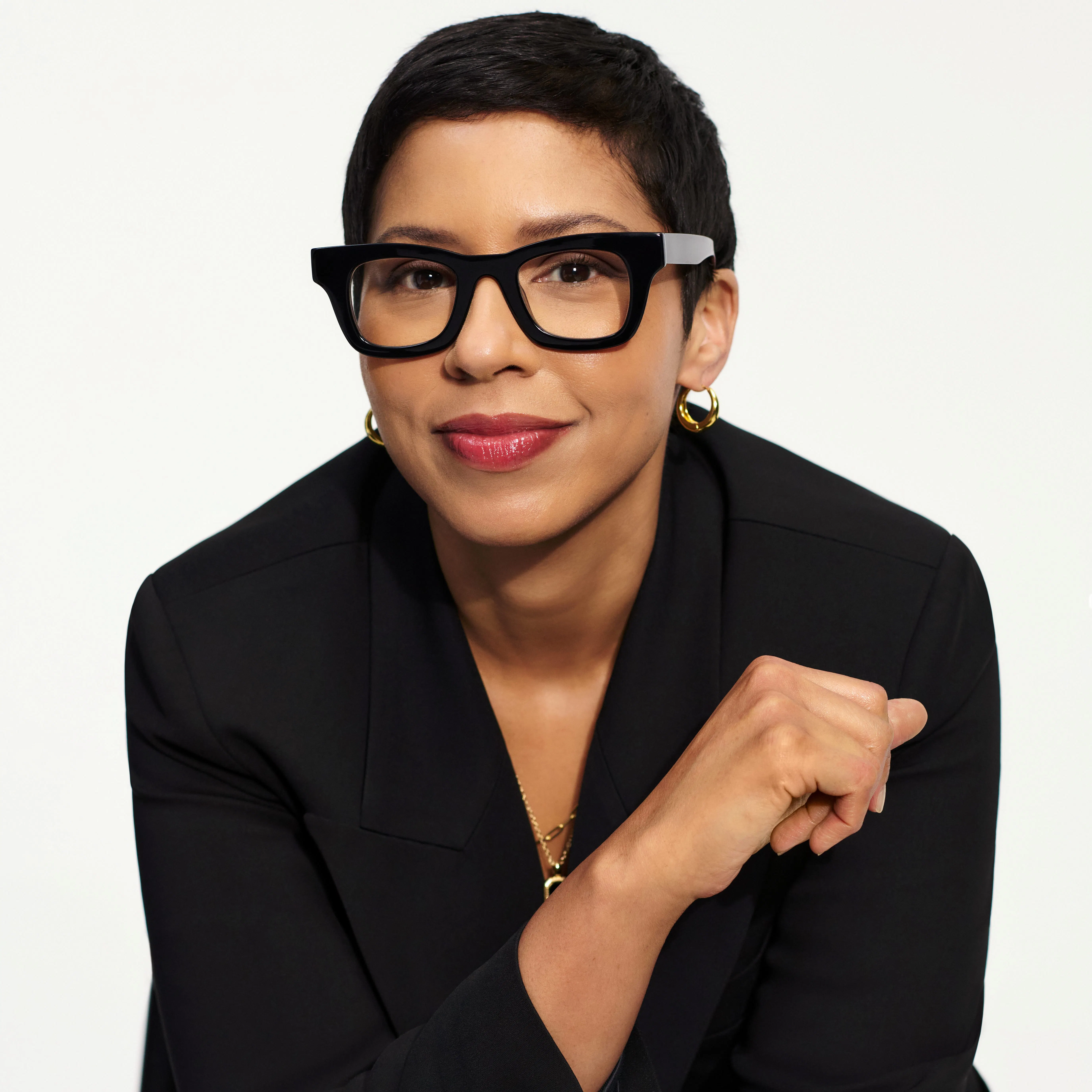 A woman with short black hair, think black glasses, and a black suit
